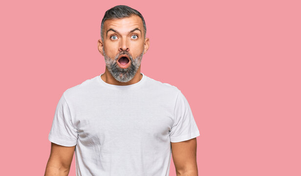 Middle age handsome man wearing casual white tshirt afraid and shocked with surprise and amazed expression, fear and excited face.