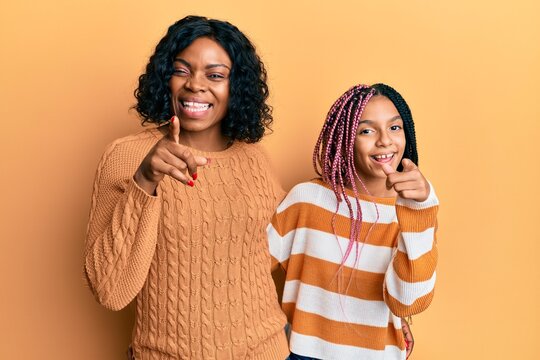 Beautiful african american mother and daughter wearing wool winter sweater pointing fingers to camera with happy and funny face. good energy and vibes.