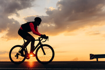 Fototapeta na wymiar Side view of road cyclist training during amazing sunset