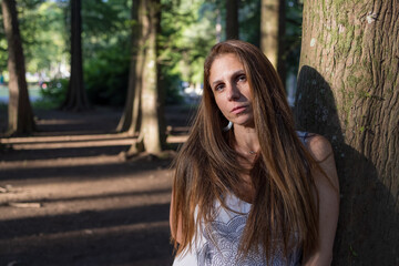 Retrato de mulher branca de 45 anos com cabelos castanhos. Arvores e raios solares.