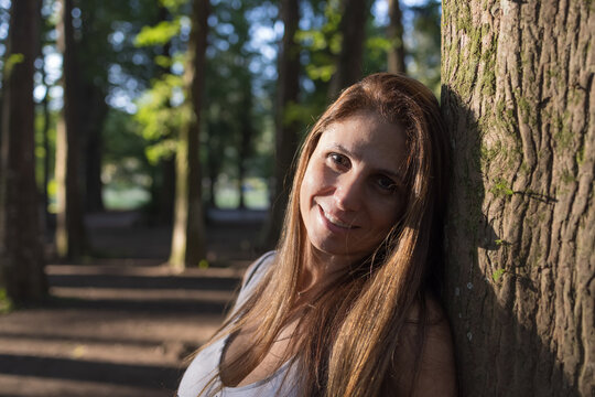 Retrato de mulher branca de 45 anos com cabelos castanhos. Arvores e raios solares.