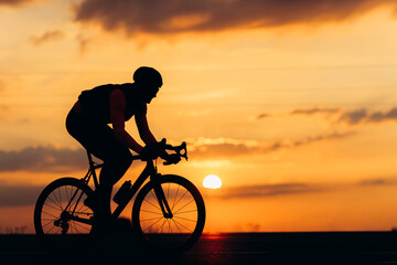 Fototapeta na wymiar Sporty man in silhouette riding bike on paved road