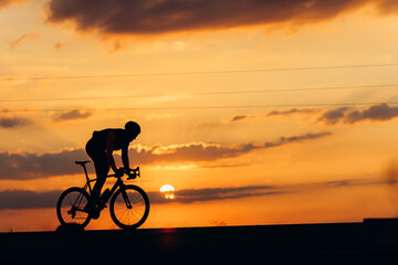 Fototapeta na wymiar Muscular man biking on road during amazing sunset