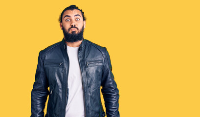 Fototapeta premium Young arab man wearing casual leather jacket puffing cheeks with funny face. mouth inflated with air, crazy expression.