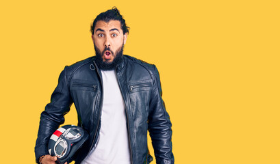 Young arab man holding motorcycle helmet scared and amazed with open mouth for surprise, disbelief face