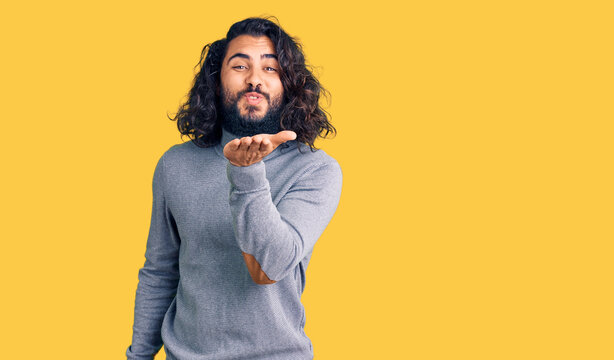 Young arab man wearing casual clothes looking at the camera blowing a kiss with hand on air being lovely and sexy. love expression.