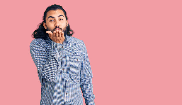Young arab man wearing casual clothes looking at the camera blowing a kiss with hand on air being lovely and sexy. love expression.