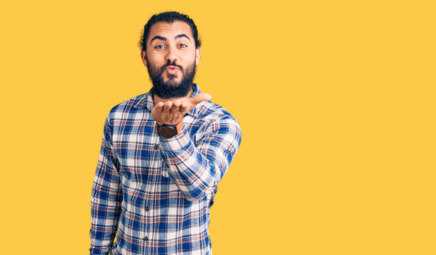 Young arab man wearing casual clothes looking at the camera blowing a kiss with hand on air being lovely and sexy. love expression.