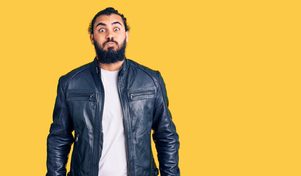 Young arab man wearing casual leather jacket puffing cheeks with funny face. mouth inflated with air, crazy expression.
