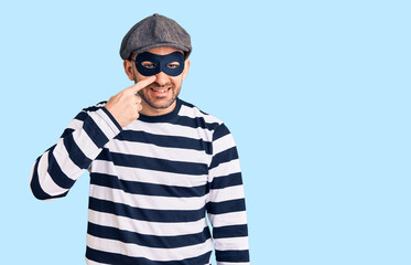 Young handsome man wearing burglar mask pointing with hand finger to face and nose, smiling cheerful. beauty concept