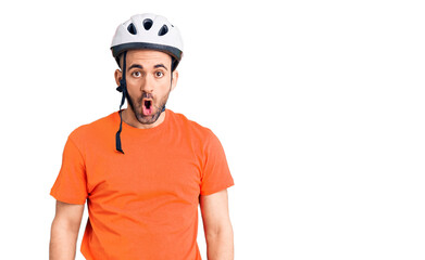 Young handsome man wearing bike helmet scared and amazed with open mouth for surprise, disbelief face