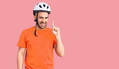 Young handsome man wearing bike helmet pointing finger up with successful idea. exited and happy. number one.