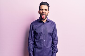 Obraz premium Young handsome man with beard wearing casual shirt sticking tongue out happy with funny expression. emotion concept.