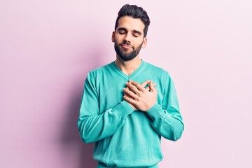 Young handsome man with beard wearing casual sweater smiling with hands on chest, eyes closed with grateful gesture on face. health concept.