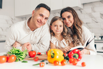 Happy family of little girl and her parents having fun and cooking salad in kitchen at home.