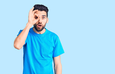 Fototapeta premium Young handsome man with beard wearing casual t-shirt doing ok gesture shocked with surprised face, eye looking through fingers. unbelieving expression.