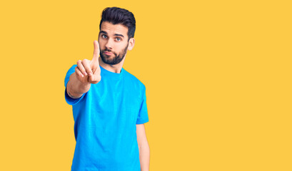 Young handsome man with beard wearing casual t-shirt pointing with finger up and angry expression, showing no gesture