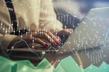 Double exposure of businesswoman hands typing on computer and financial graph hologram drawing....