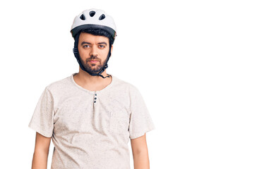 Young hispanic man wearing bike helmet with serious expression on face. simple and natural looking at the camera.