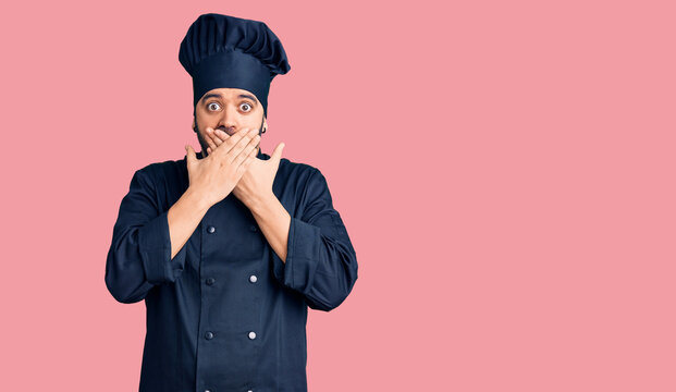 Young hispanic man wearing cooker uniform shocked covering mouth with hands for mistake. secret concept.