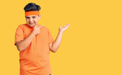 Little boy kid wearing sportswear amazed and smiling to the camera while presenting with hand and pointing with finger.