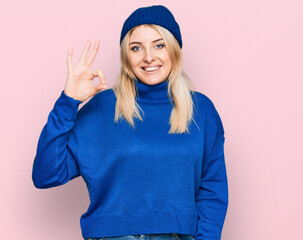 Obraz na płótnie Canvas Young caucasian woman wearing wool winter sweater and cap smiling positive doing ok sign with hand and fingers. successful expression.