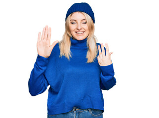 Obraz na płótnie Canvas Young caucasian woman wearing wool winter sweater and cap showing and pointing up with fingers number nine while smiling confident and happy.