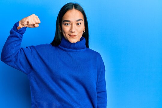 Young asian woman wearing casual winter sweater strong person showing arm muscle, confident and proud of power