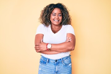 Young african american plus size woman wearing casual white tshirt happy face smiling with crossed arms looking at the camera. positive person.