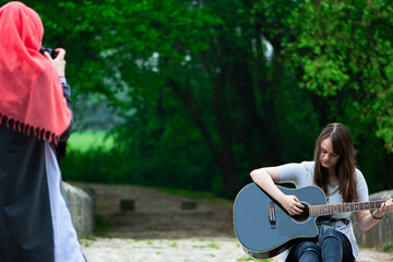 Young girl playing guitar while muslim girl taking photo of her