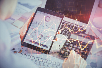 Double exposure of man's hands holding and using a digital device and forex graph drawing. Financial market concept.