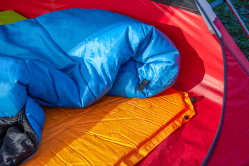 The inside of a red tent with an blue sleeping bag and an orange self-inflating blow-up mattress...