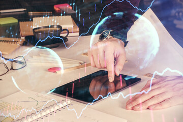 Double exposure of man's hands holding and using a digital device and forex graph drawing. Financial market concept.