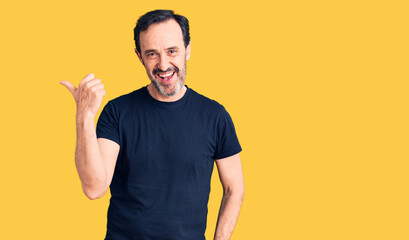 Middle age handsome man wearing casual t-shirt smiling with happy face looking and pointing to the side with thumb up.