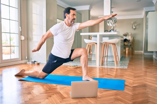 Middle age man with beard training and stretching doing exercise at home looking at yoga video on computer