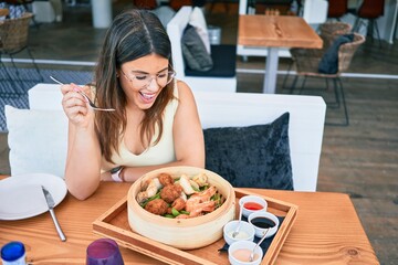 Young beautiful hispanic woman smiling happy. Sitting on the table eating food at restaurant