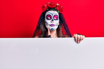 Young woman wearing day of the dead costume holding blank empty banner serious face thinking about question with hand on chin, thoughtful about confusing idea