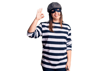 Young beautiful brunette woman wearing burglar mask smiling positive doing ok sign with hand and fingers. successful expression.