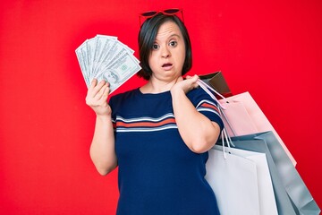 Brunette woman with down syndrome holding shopping bags and dollars clueless and confused expression. doubt concept.