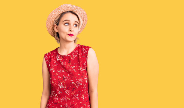 Young beautiful blonde woman wearing summer hat smiling looking to the side and staring away thinking.