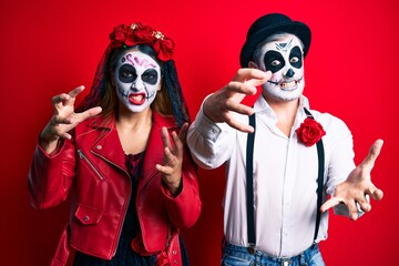 Couple wearing day of the dead costume over red shouting frustrated with rage, hands trying to strangle, yelling mad