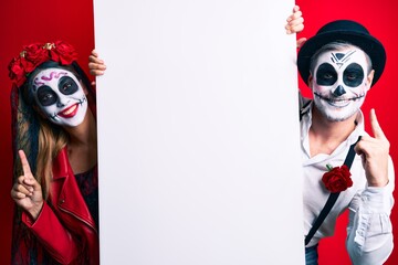 Couple wearing day of the dead costume holding blank empty banner surprised with an idea or question pointing finger with happy face, number one