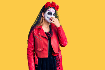 Woman wearing day of the dead costume over background smelling something stinky and disgusting,...