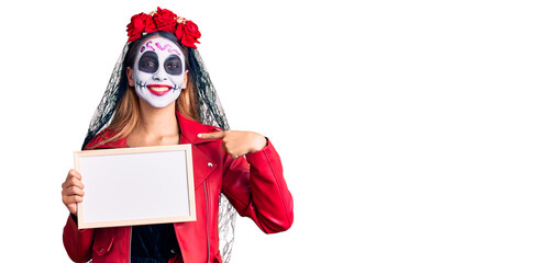 Woman wearing day of the dead costume holding empty white chalkboard pointing finger to one self smiling happy and proud