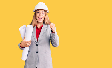Beautiful young woman wearing architect hardhat holding build project screaming proud, celebrating victory and success very excited with raised arms