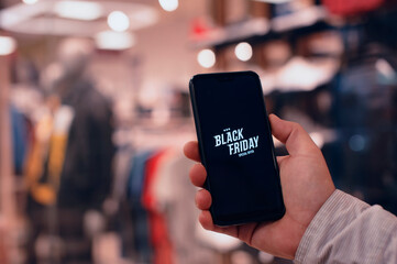 Online shopping on Black Friday. A man holds a smartphone in his hands against the background of a fashionable clothing boutique.