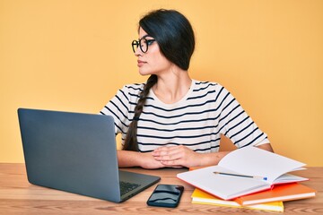 Brunette teenager girl working at the office with laptop looking to side, relax profile pose with natural face with confident smile.