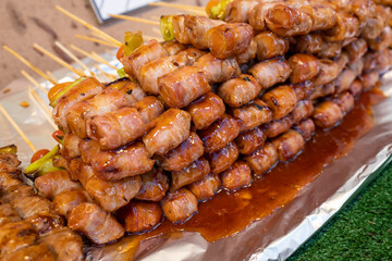 Thai street food, marinated small sausage wrapped in bacon on a skewer with a chili and tomato