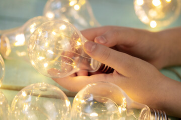 children's hand with a decorative light bulb garland on a light wooden surface