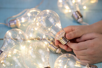children's hand with a decorative light bulb garland on a light wooden surface